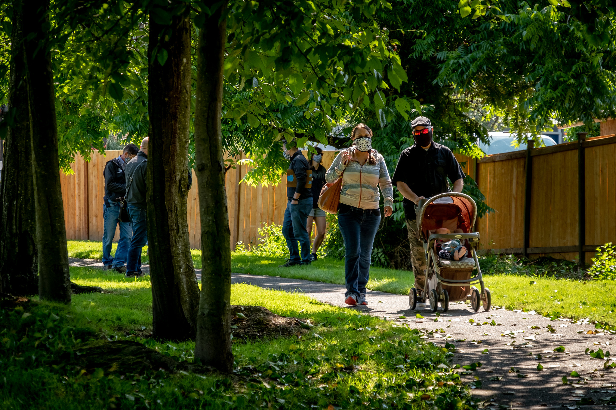 A couple with a baby in a stoller walk along a tree-lined path.