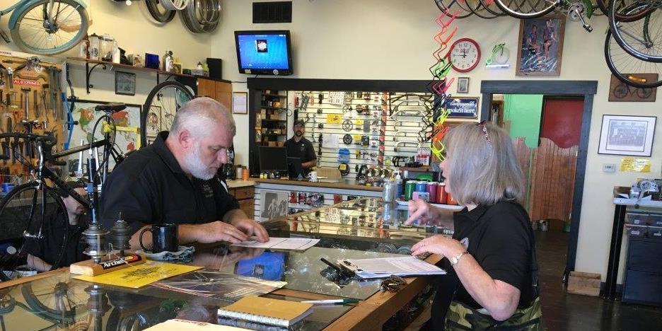 Two people talk across a counter top in a bike shop