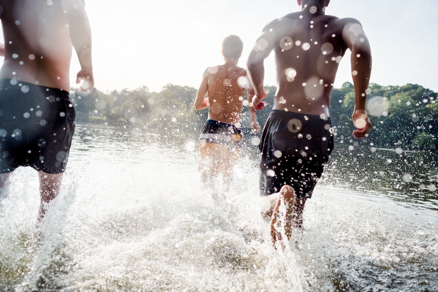 Three men running and splashing in shallow water at a lake