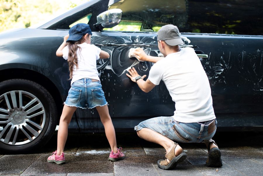 A father and daughter washing a black car with soapy sponges