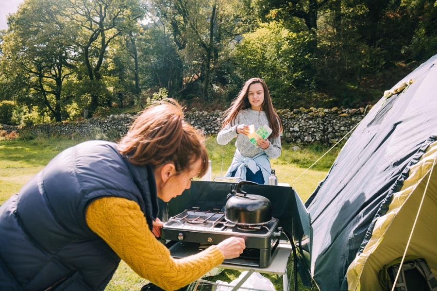 A woman lighting a camp stove with a teenage girl and tent in the background