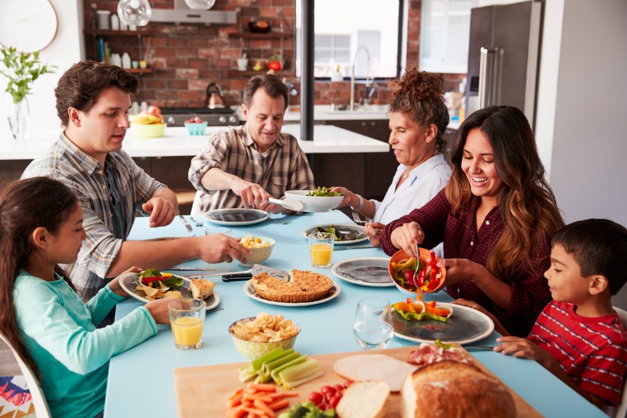 A family of adults and children sit at a table filled with holiday food
