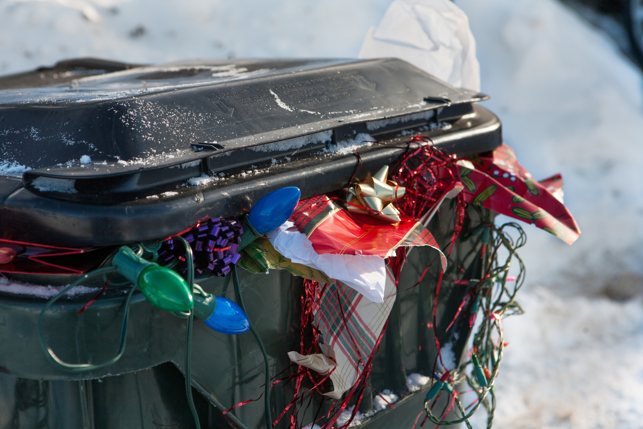 A green trash can overflows with festive holiday garbage.