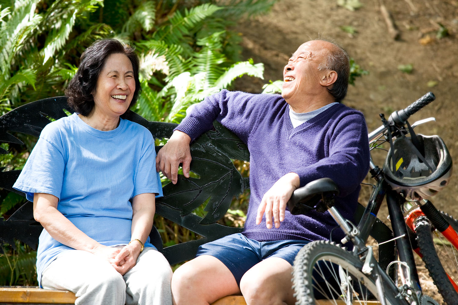 An older woman and man laugh while sitting on a park bench