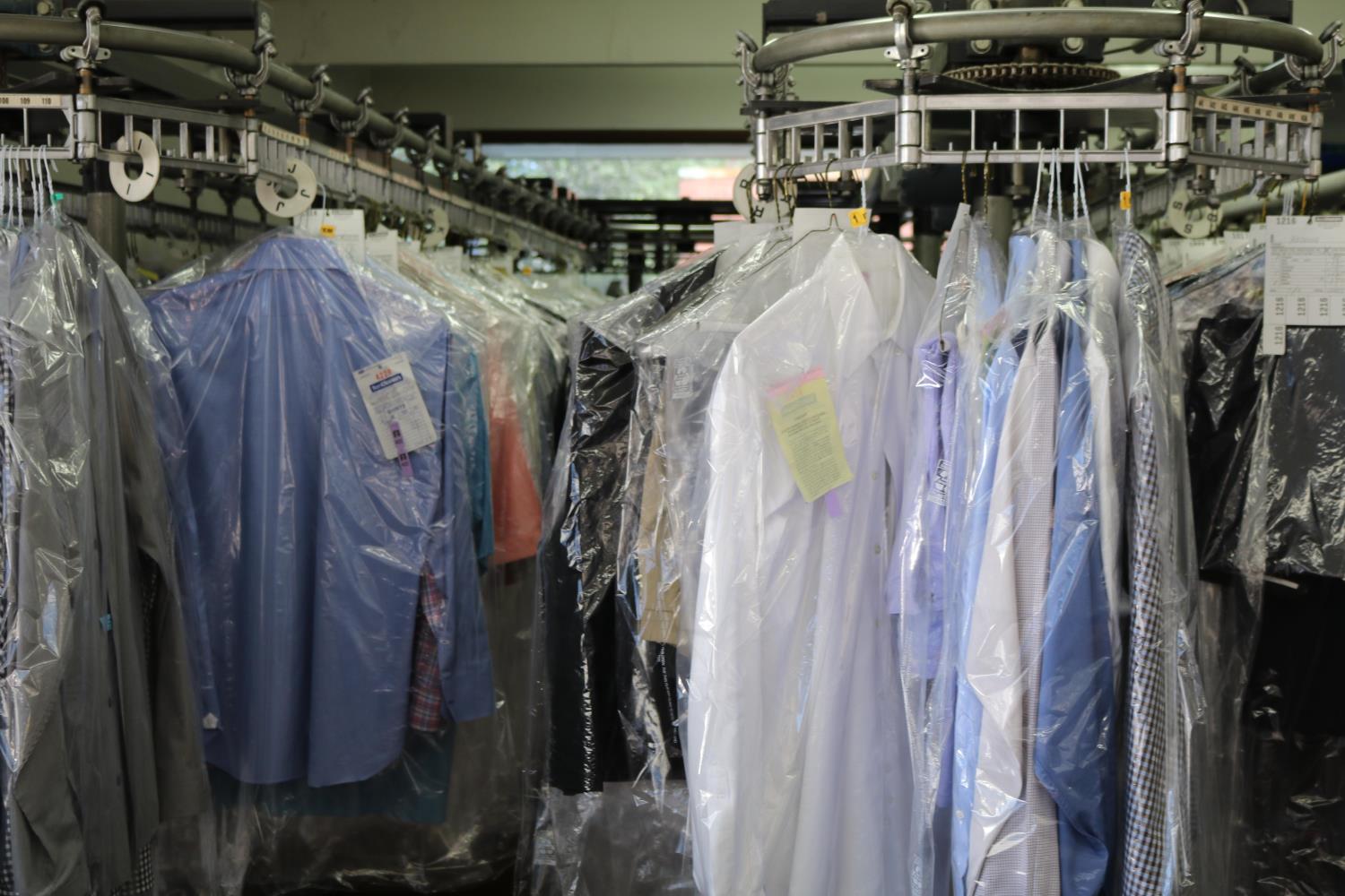 Several hanging blue, white, and neutral colored dress shirts are individually wrapped in plastic wrap at a dry cleaning business