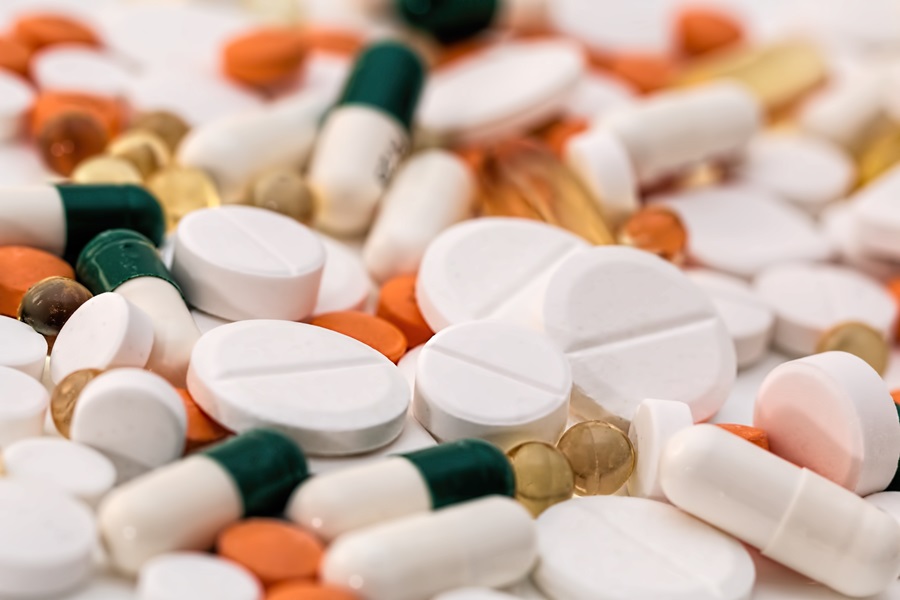An image of arious pills spread on a surface, including large white pills, small orange pills, blue and white capsules