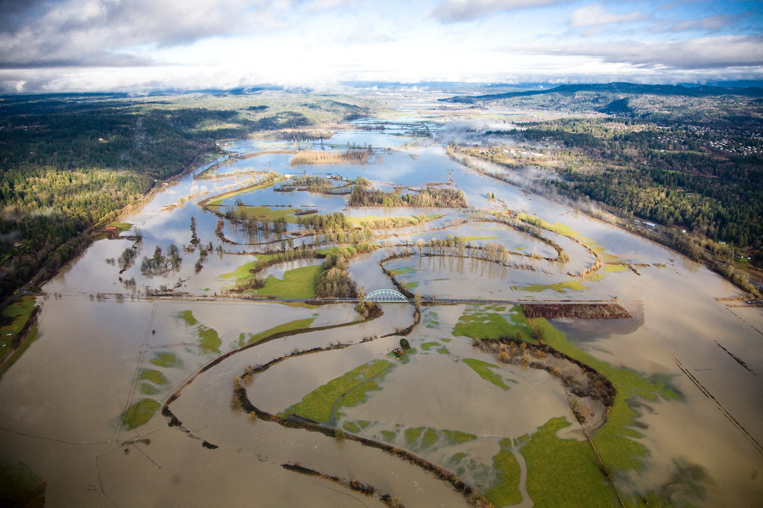 An aerial image of the Snoqualmie River valley that has flooded entirely, with brown flood waters extending into farmland beyond banks of river.