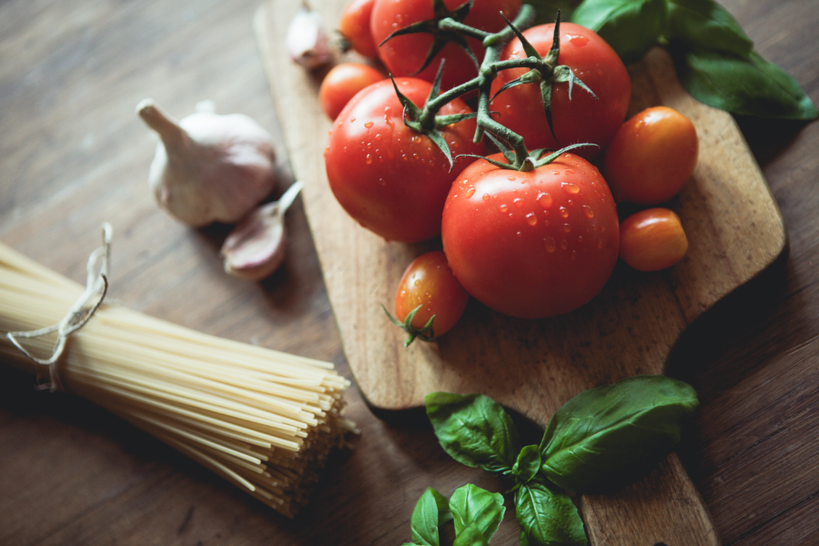Large red tomatoes, small orange tomatoes, and garlic on a wooden serving board on a table