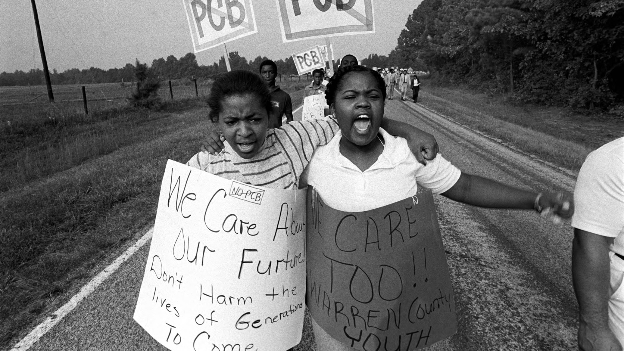 Two Black youth with arms around each other participate in a protest in Warren County. They have signs that say, "We care about our future."