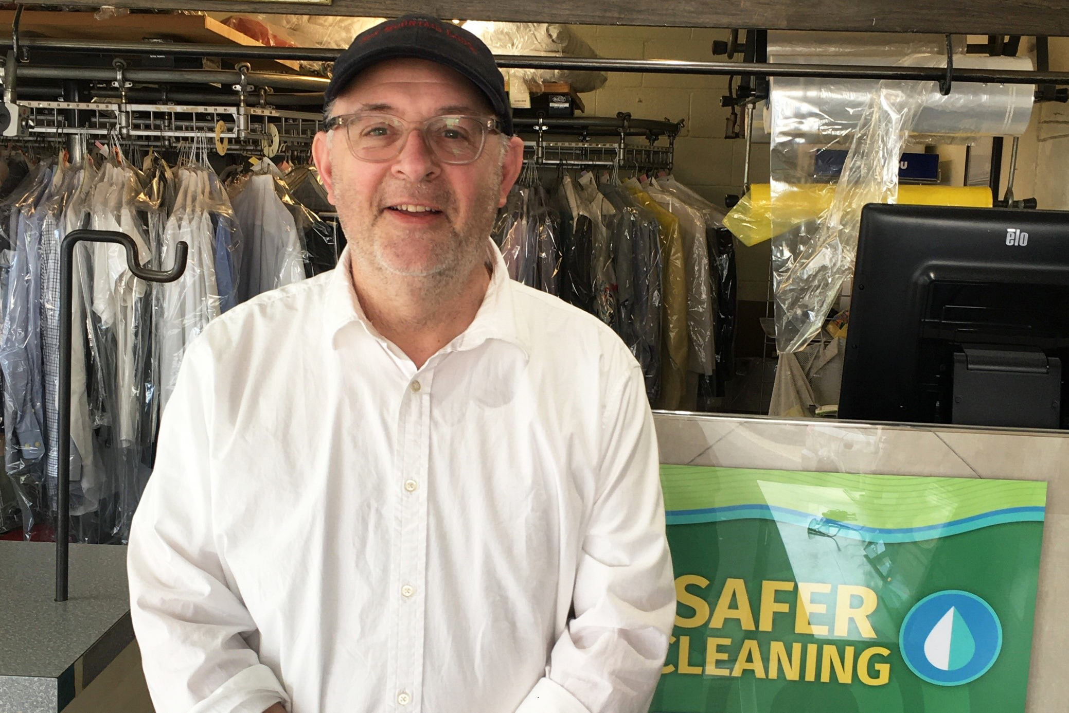 Man wearing dark hat and white shirt stands in a dry cleaning shop