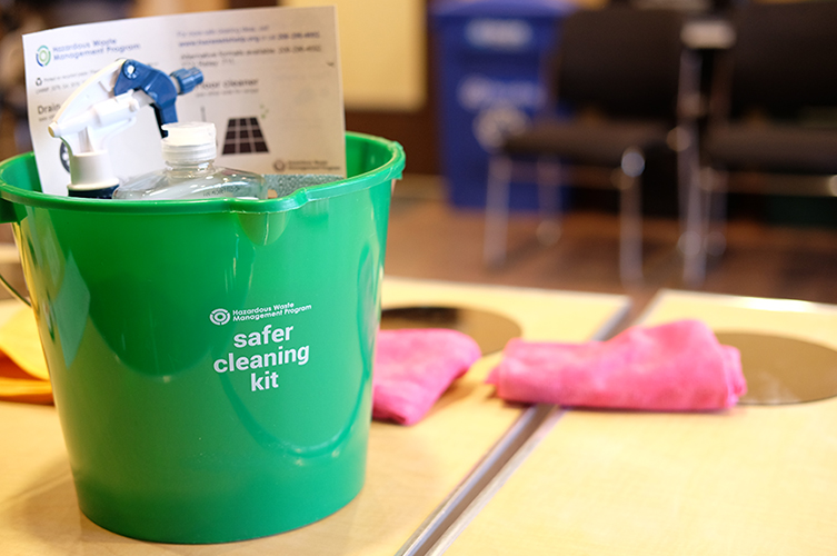 A green bucket that is filled with materials for a safer cleaning kit.