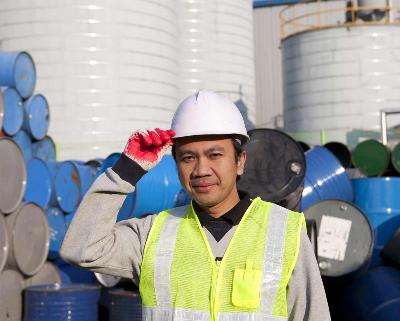 Man wearing safety vest and hard hat stands in front of barrel containers