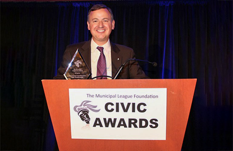 Councilmember Dembowski speaking at a podium with a sign on the front reading Civic Awards.