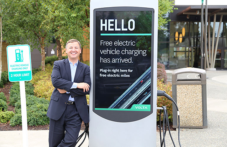 Councilmember Dembowski leans against a charging station. Text on the station's screen reads - Hello, free electric vehicle charging has arrived.