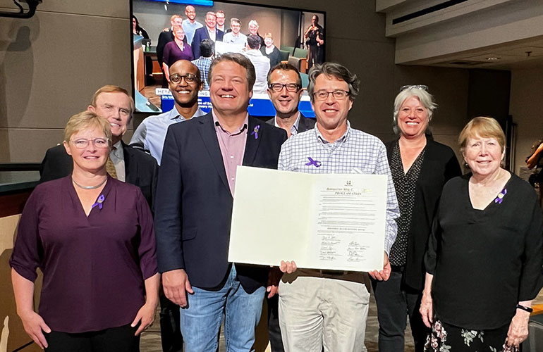 Councilmembers Perry, von Reichbauer, Zahilay, Dunn, McDermott, Balducci and Kohl-Welles pose with a community member who holds the recognition document.
