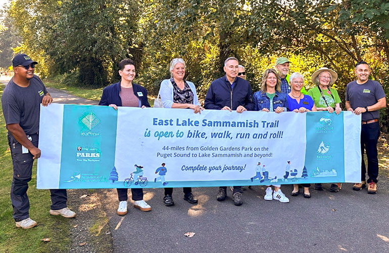 Councilmembers, Executive, and others hold banner that says "East Lake Sammamish Trail is open to bike, walk, run and roll!".