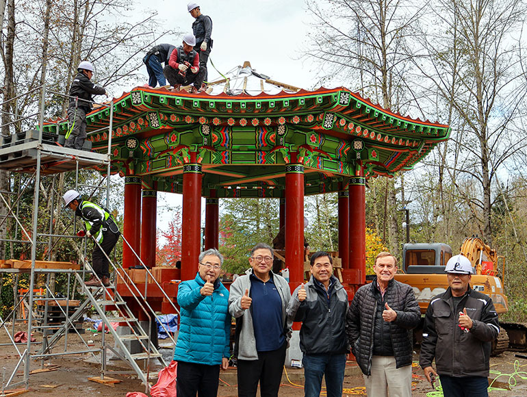 Workers on top of pagoda and group standing in front on the ground.