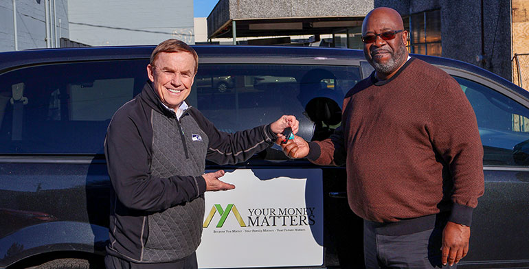 Standing in front of van with Your Money Matters sign on the van's side.