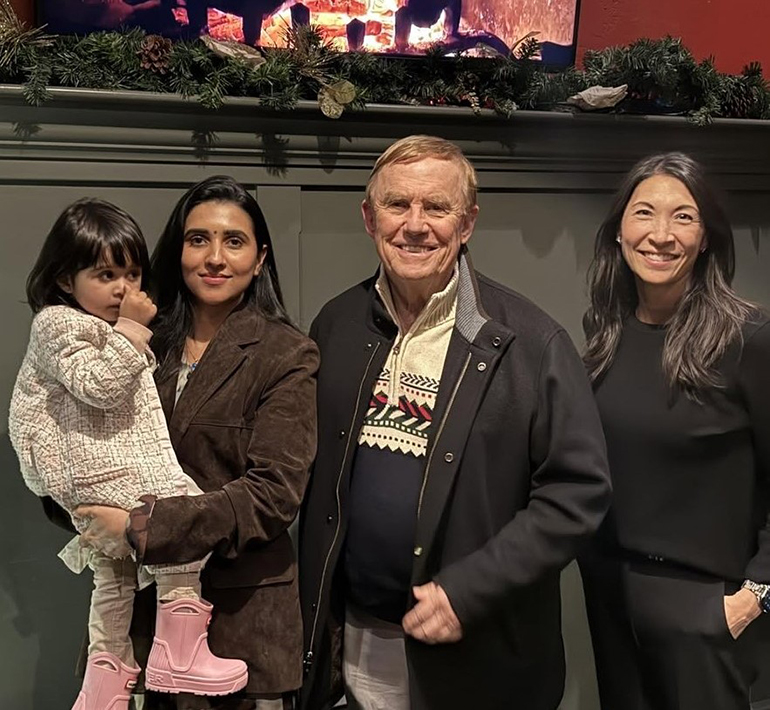 A child is held by an adult, with two other adults standing beside them.