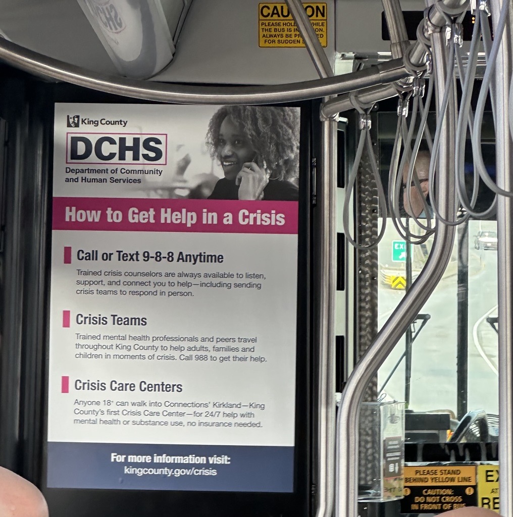 Image of the interior of a King County Metro bus showing an advertisement for how to access help in a crisis.