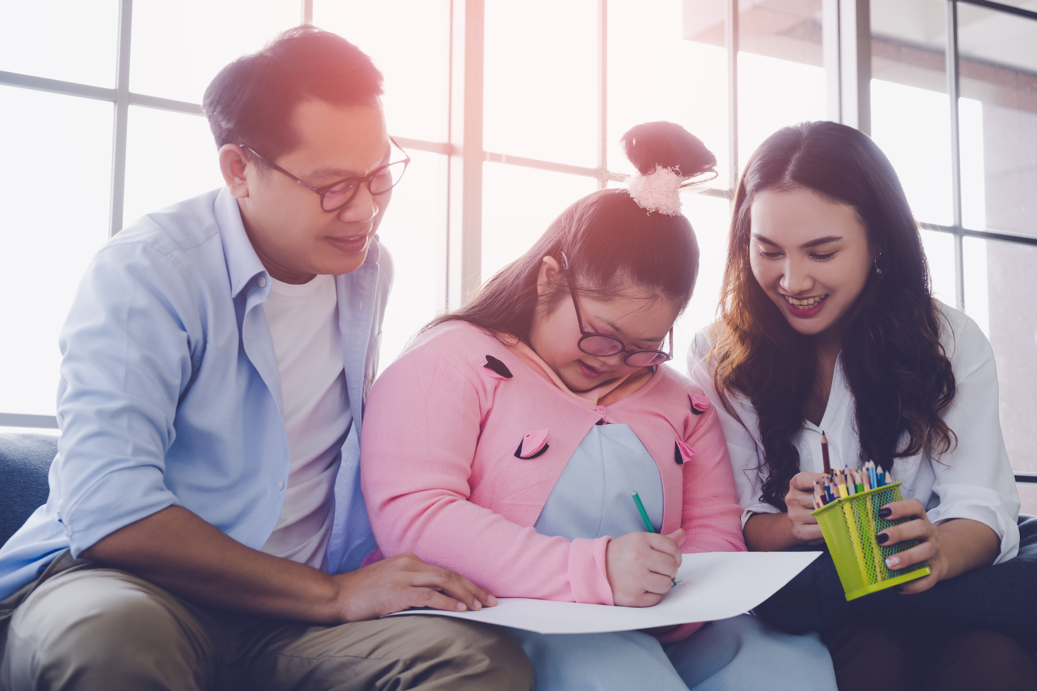 A father sitting with his daughter and a therapist on a couch, working on a document together. The daughter has Down Sydrome.