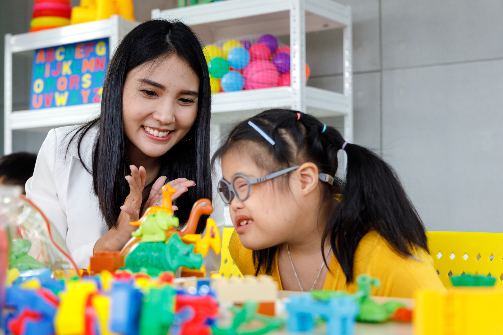 A young Asian woman who is helping a young Asian toddler girl to play with colorful shapes.