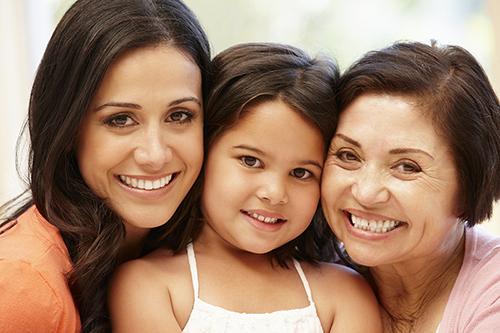 A young child is smiling between two smiling women.