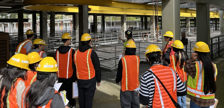 A group of people in reflective orange vests and hard hats are touring a treatment plant