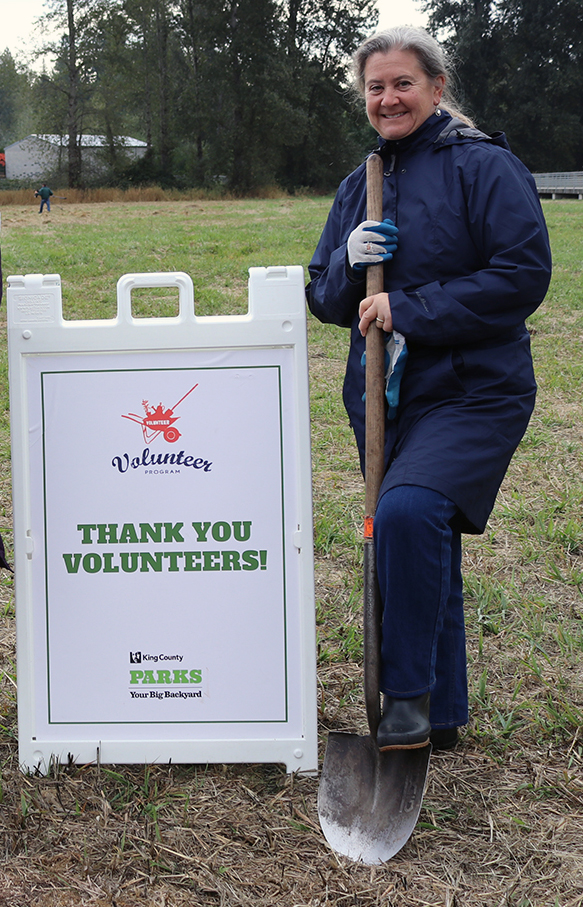Christie True stands with a shovel beside a sign saying, Thank You Volunteers!