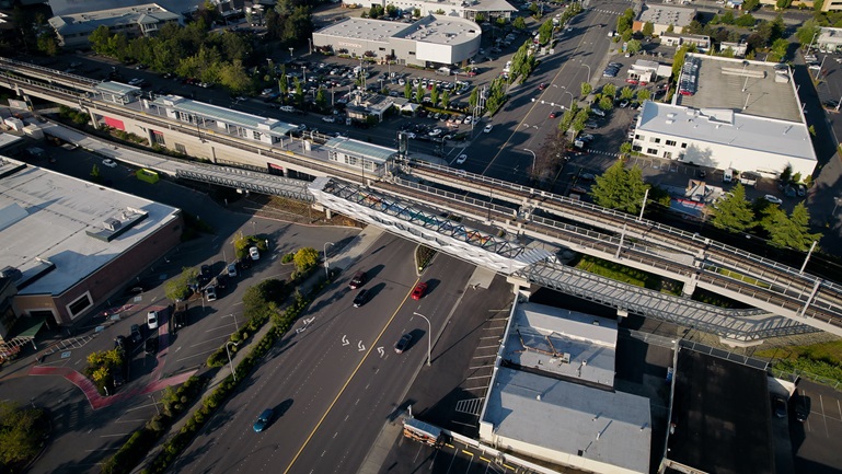 Aerial photo of a bridge crossing over a road. Flat roof buildings are to either side of the bridge.