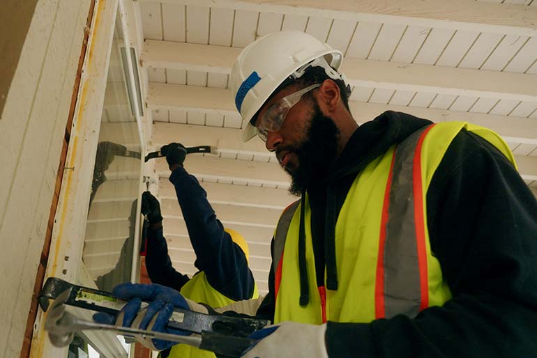 Workers recovering windows from a house undergoing deconstruction