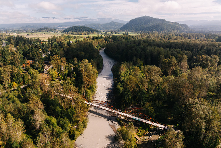 Aerial photo of the White River and the White River Bridge surrounded by trees, with mountains in the background.