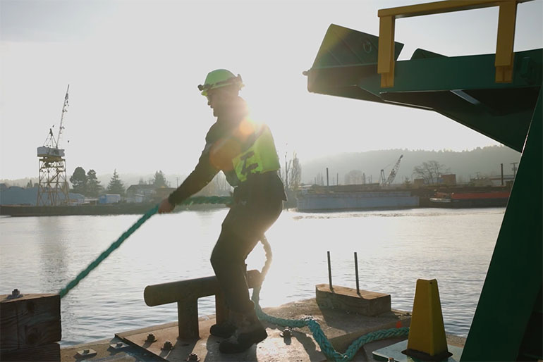 Dock worker handling the lines to tie up a barge filled with polluted sediment from the Duwamish Waterway
