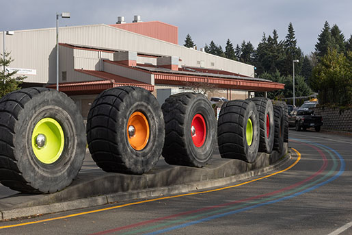 Art installation along the entrance road to a transfer station, featuring big truck tires and colorful wheels
