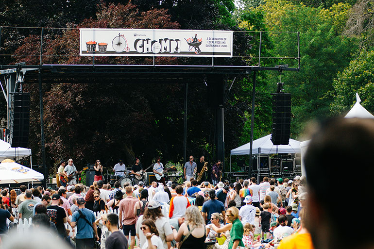 Musicians on stage at Chomp with a crowd of people on the grass