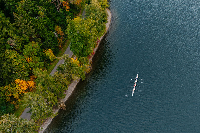 Aerial photo of a scull on Lake Washington near the treed shore of Seward Park 