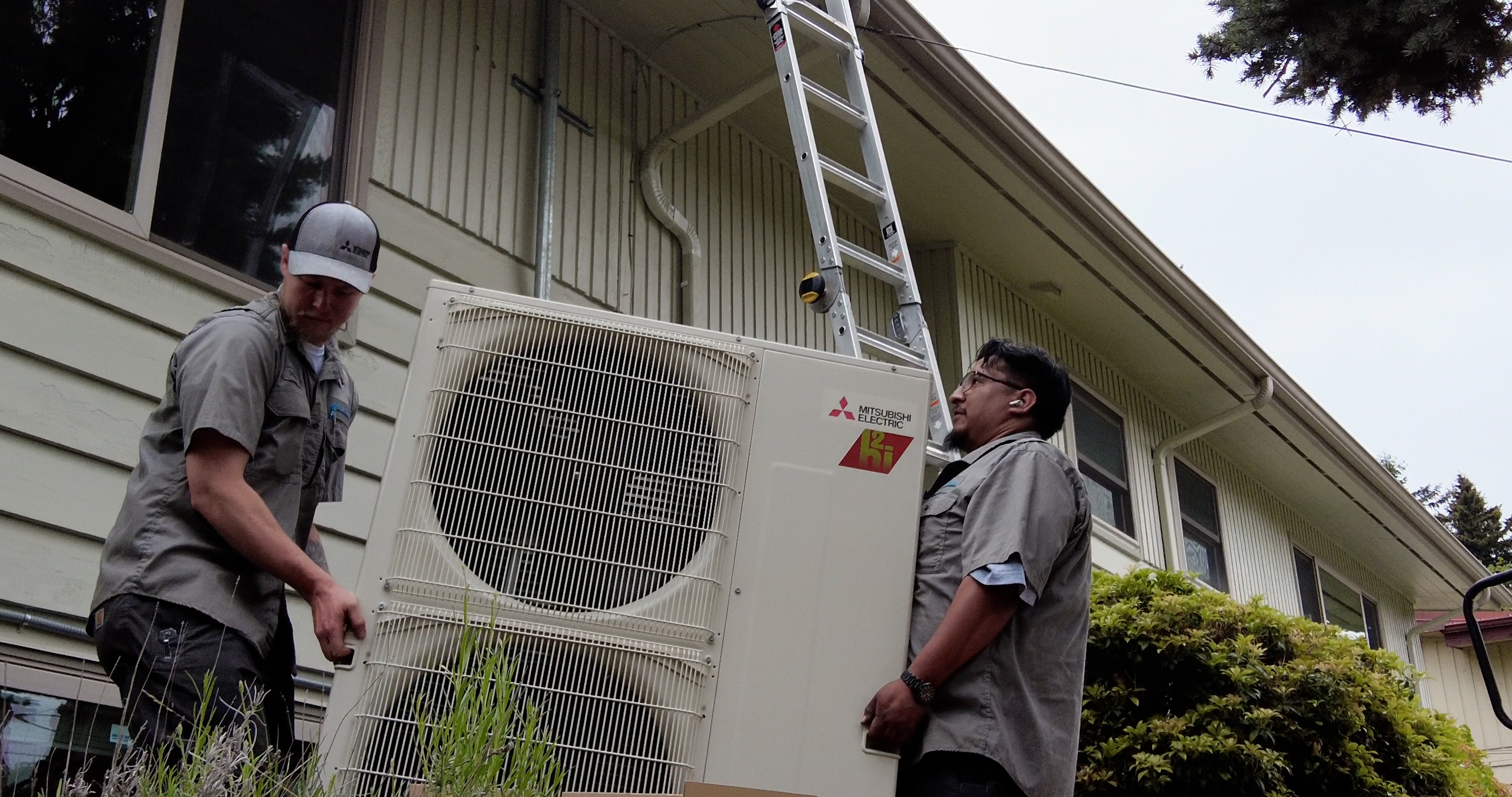 contractors carry a heat pump toward a home