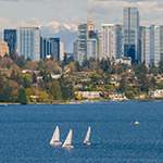 Sailboats on bright blue waters of Lake Washington with buildings of the Bellevue skyline in the background