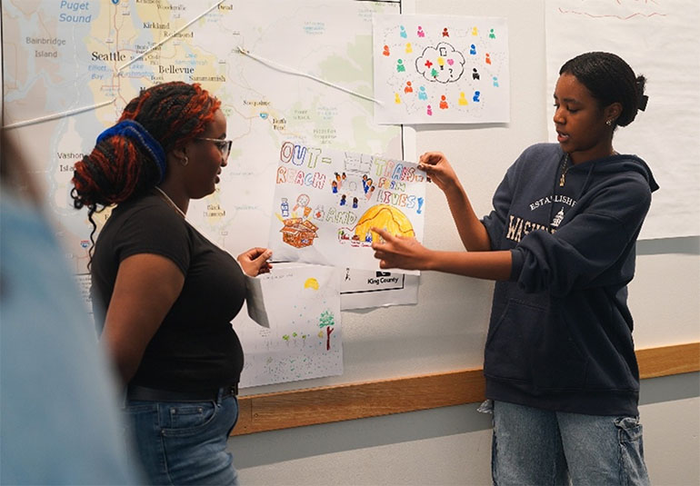 two people attach a piece of art to a map