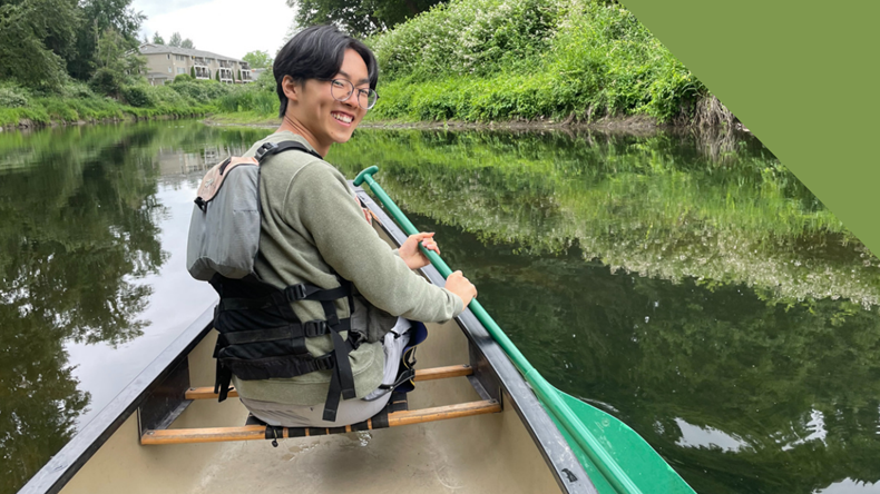 smiling man paddling in water surrounded by trees