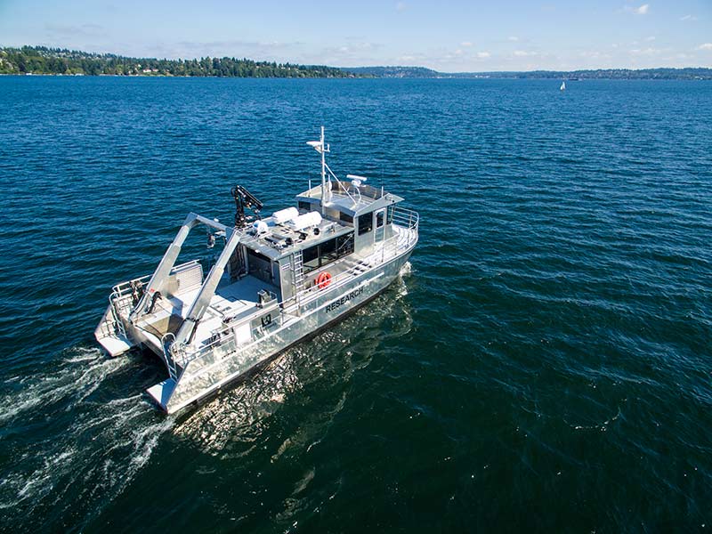 An aerial view of the R/V SoundGuardian cruising on Lake Washington with wooded land in the distance.