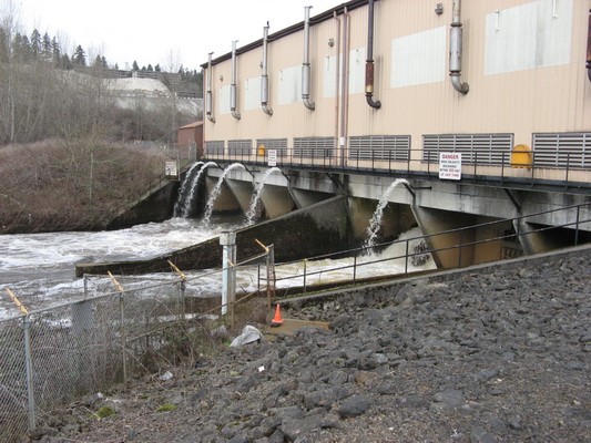 A tan building sits above a river with water spouting from several places along it.