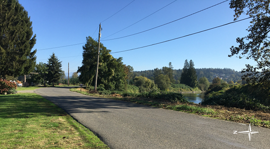 A paved road with a river to the right and blue sky.