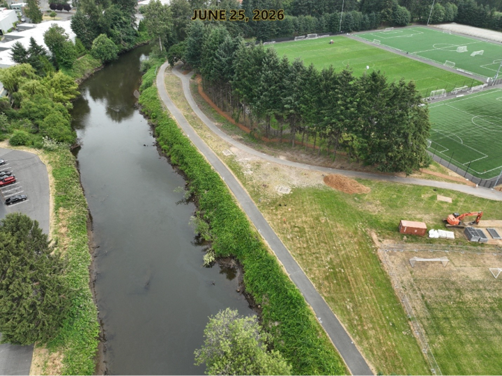 River with damaged levee on left side. Trails and soccer fields on right side. 