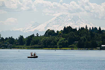 A small boat on Lake Washington, with a tree-lined shore in the background and Mount Rainier beyond.