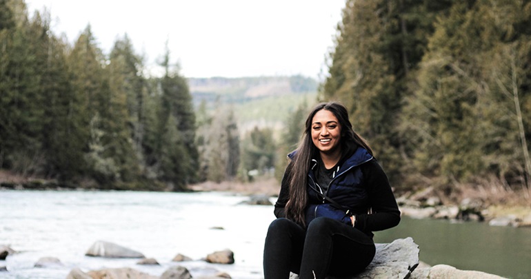 Woman sitting on a river rock by the water's edge