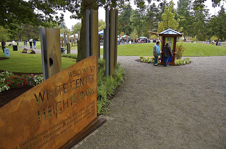White Center Heights park sign, kiosk and play area surrounded by grass