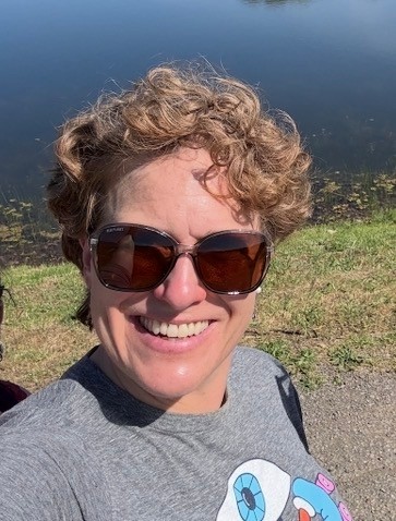 A person in short hair and sunglasses smiling outside