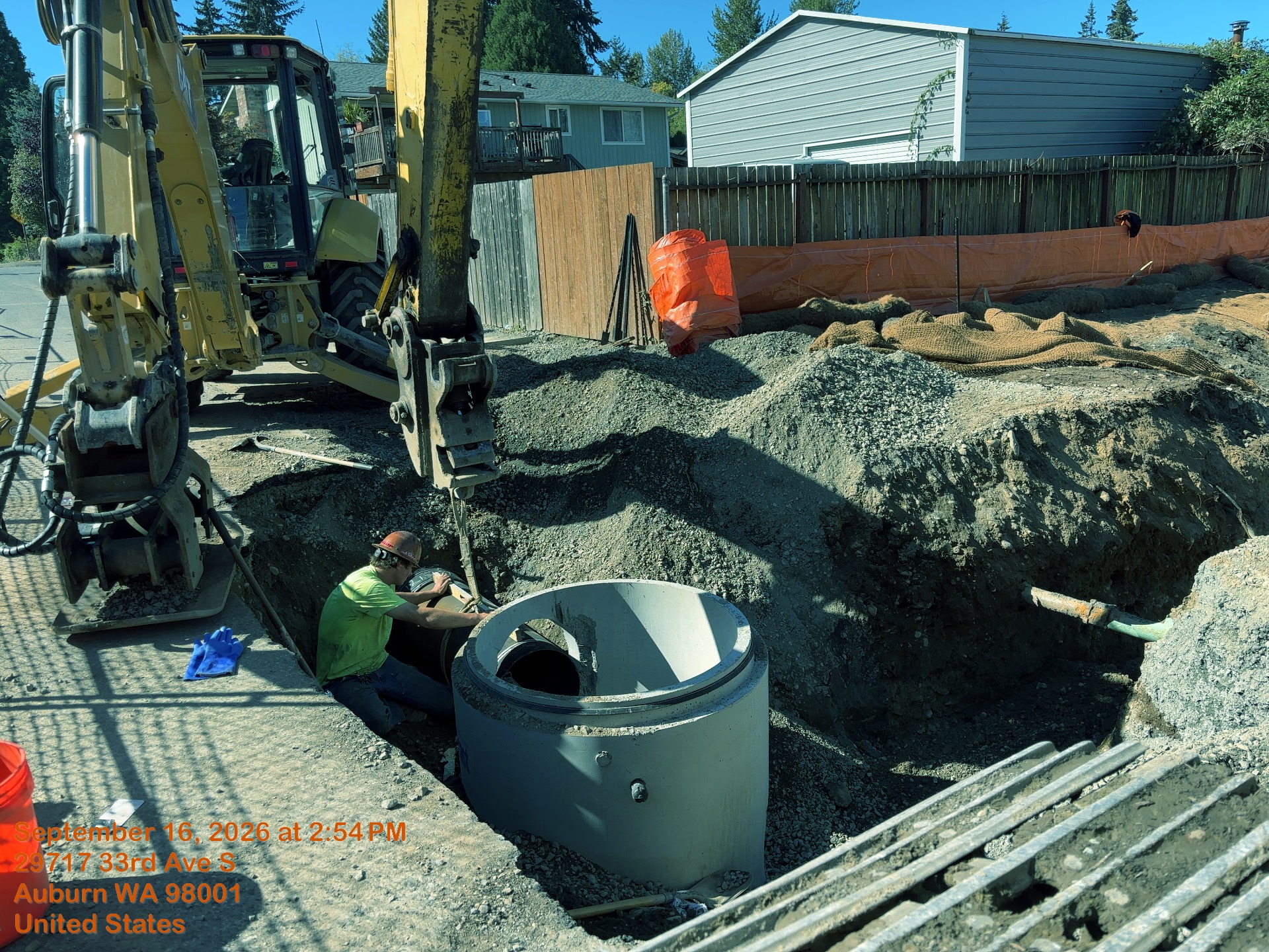 Excavator is helping connect a stormwater pipe to a concrete basin in an open trench. 