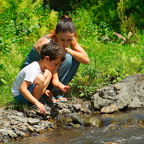 A mother and child crouch beside a stream looking at something in mother's hand